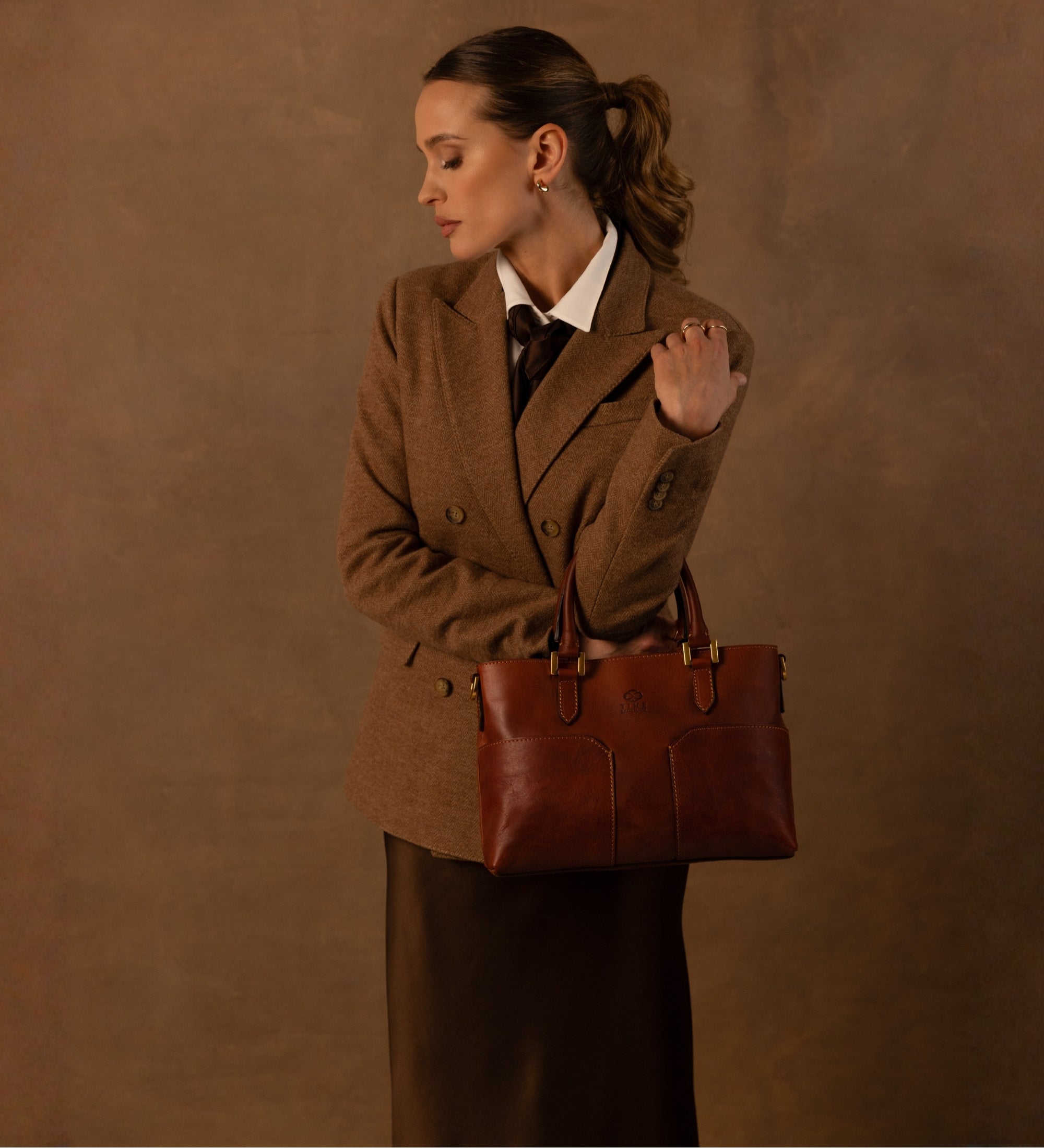 Frau in Tweed-Blazer steht mit der cognacbraunen Camilla Schultertasche in der Hand