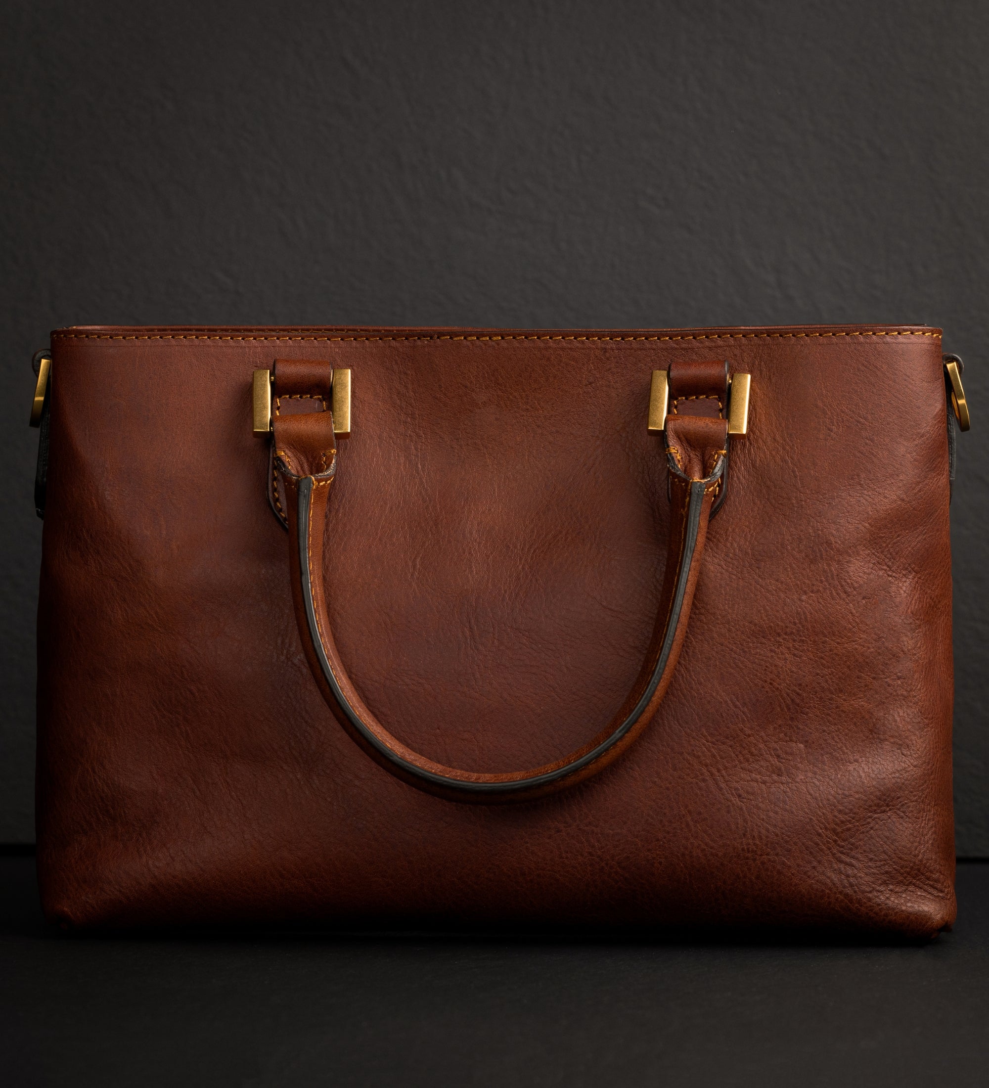 Cognacbraune Camilla Schultertasche schräg gezeigt vor dunklem Hintergrund